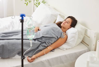 Damardan damlayan genç bir kadın klinikteki rahat tıbbi kanepede serumla yatıyor vitamin aşılamak için hastane terapisi sağlığını korumak için ilaçlar, kemoterapi kanser tedavisi...
