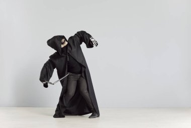 Ölüm meleği kostümlü komik adam elinde siyah başlıklı ve iskelet maskeli tırpanla stüdyonun gri arka planında fotokopi çekerek eğleniyor. Cadılar Bayramı partisi ve korku konsepti