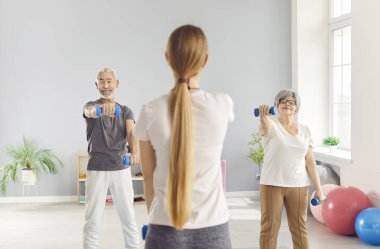 Rehabilitasyon merkezinde yaşlı bir çift, dambıllarla jimnastik yapıyor. Bir bayan eğitmen yaşlı insanlara öğretir. Yaşlı çift kavramı, spor eğitimi, fizik tedavi.