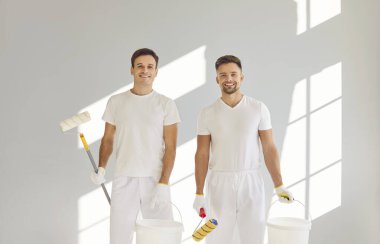 Gülümseyen mutlu boyacı takımı ellerinde boya ruloları ve kovalarla kameraya bakıyor ve yeni dairenin duvarını boyayacaklar. Müteahhitler tadilat yapıyor. Taşınmaya hazırlanıyorlar..