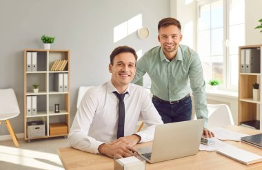 İki mutlu, kendine güvenen iş adamının portresi. İş yerinde kameraya neşeli bakan gömlekler giyiyorlar. Masada oturuyorlar. Şirket çalışanları ve erkek iş arkadaşları ofiste çalışıyor..