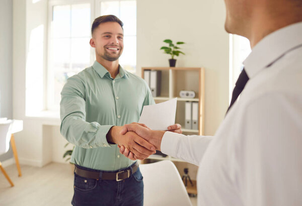 Two happy young men shaking hands and smiling. Two people meet in the office, establish partnership relations, make a lucrative business deal and exchange handshakes. Cooperation, teamwork concept