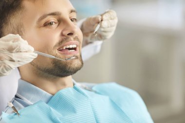 Doktor dişçi, klinik ziyareti sırasında bir hastaya bakarken diş aletini kullanarak ağız kontrolü yapar. Diş hekimliğinde yapılan rutin muayenenin bir parçası olarak uygun diş bakımı ve hijyen.