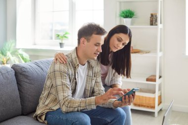 Mutlu aile çifti evde birlikte dinlenmekten hoşlanır, online eğlence için bir cep telefonu kullanır. İnternete bağlanıyorlar, boş zamanlarını birlikte rahatlayarak geçiriyorlar..