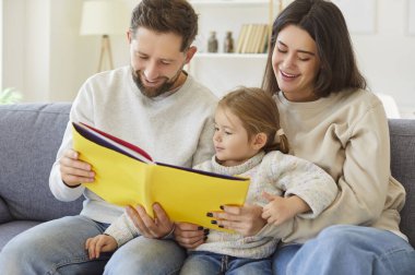 Mutlu ebeveynler ve küçük kızlar evde birlikte kitap okuyarak birbirlerine bağlanıyorlar. Boş zaman aktivitesi öğrenmeyi, aile bağlarını ve sıcak, rahatlatıcı bir ortamda geçirilen kaliteli zamanı teşvik eder..
