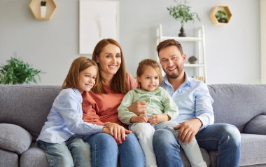 Mutlu gülümseyen ebeveynlerin portresi evdeki oturma odasındaki kanepede oturan ve hafta sonları birlikte vakit geçirmekten zevk alan iki çocuk ve kız çocuğuyla birlikte. Mutlu aile ve eğlence konsepti.
