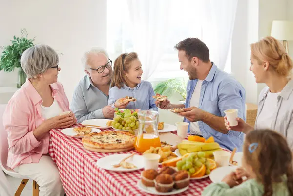 Mutlu büyük aile toplantısı, masada yemek yemek, evde üç nesil birlikte gülmek, partide buluşmaktan keyif almak, lezzetli yemekler yemek, ebeveynler, büyükanneler, çocuklar.