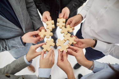 Tahta yapboz yapan bir grup iş adamının elleri. İş arkadaşları, ofis içindeki yapboz parçalarına katılıp proje üzerinde birlikte çalışıyorlar. Takım çalışması konseptinde destek.