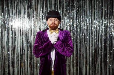 Mor kostümlü, şaşkın ve şaşkın bir adamın portresi. Parlak bir arka planda, bir parti sırasında. Şenlikli kutlamalar eğlence, anlamlı duygular ve canlı bir akşam atmosferi içerir..