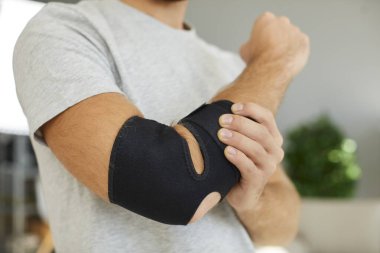 El yaralanması. Yarası iyileşmekte olan adamın dirseğinde siyah elastik destekleyici tıbbi bandaj yakın çekim. Kırık kemik ya da spor sakatlığı sonrası koluna sargı bezi takmak zorunda kalan bir adam..