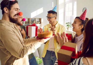 Mutlu genç insanlar pasta hediye ediyor. Gülümseyen erkek arkadaşı doğum günüyle selamlıyorlar. Coşkulu çok ırklı gençler erkek arkadaşını yıldönümünde tebrik ediyor. Kutlama ve ayrılık kavramı.