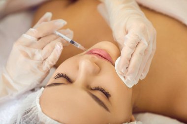 Güzeller güzeli bir kadın güzellik kliniğinde dudak büyütme ameliyatı sırasında dudaklarına iğne vurulur. Eldivenli güzellik uzmanının elleri genç kadınların yüzüne güzellik iğnesi yapıyor. Güzellik konsepti.
