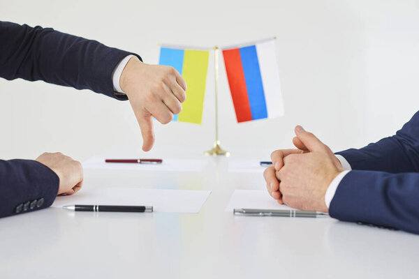 Strained relations between Ukraine and Russia. Representative of Ukrainian side at talks expresses his dissatisfaction by pointing his thumb down. Close up of hands of diplomats near flags of states.