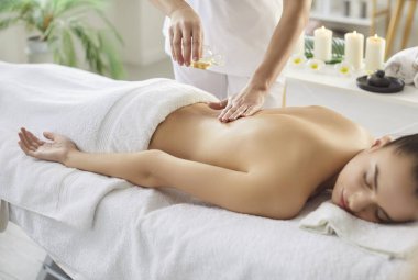 Masaj masasına uzanmış, beyaz havluyla kaplanmış aromaterapi ile masaj yapmaya hazırlanan kadınlara masaj yapan terapist. Yan görüş. Vücut bakımı kavramı