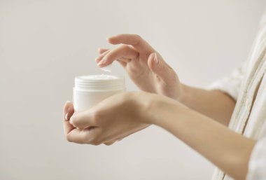 Beyaz arka planda parmak izine sahip krema dokunan genç bir kadın. Elinde nemlendirici beyaz krem olan bir kadın elinde kavanoz tutuyor. Vücut sağlığı ve cilt bakımı kavramı.