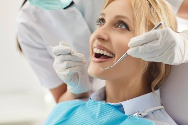 Dişçinin dişlerini incelerken dişçi koltuğunda ağzı açık oturan gülümseyen genç kadının portresini yakından çek. Düzenli ziyaretler sırasında diş hekimliği kliniğinde ağız kontrolü yapılan mutlu bir hasta..