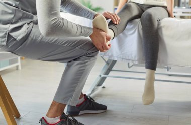 Erkek doktor osteopat ya da fizyoterapist klinikte genç bir kadının bacağını muayene ediyor. Hastayla çalışan bir fizyoterapist. Fizyoterapi ve fizik tedavi konsepti.