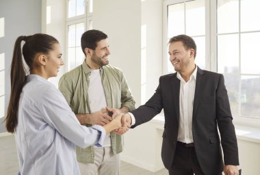 Emlakçı emlakçı genç aile çiftiyle el sıkışma anlaşması, müşterilere yeni emlak reklamları, satın almaya yardım, kiralık ev, piyasa, fiyat, ipotek, alıcı evi