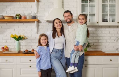 Mutlu aile portresi, iki küçük kızı olan ebeveynler, modern ev mutfağında oğlu, sevgi dolu anne ve baba kucaklaşmaları ve gülmeleri, aile haftasonunu birlikte geçirmeleri, yeni dairenin tadını çıkarmaları, 