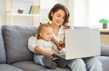 Anne ve küçük kızı evde birlikte vakit geçiriyorlar. İnternette eğlence ve internet aktiviteleri için dizüstü bilgisayar kullanırken rahat bir aile ortamında kanepede dinlenmek..