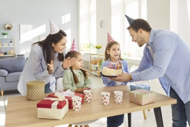 Evde doğum günü kutlayan çocukları olan pozitif ve neşeli bir aile. Kızım parti sırasında pastaya mum üflüyor. Etrafı mutluluk, neşe ve şenlikli bir atmosferle çevrili..