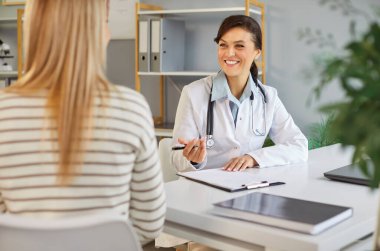 Klinikteki sağlık randevusu sırasında gülümseyen dostane bir doktor genç bayana danışıyor. Muayeneden sonra kadın hastayla tıbbi sonuçları tartışan profesyonel bir doktor ya da kardiyolog.