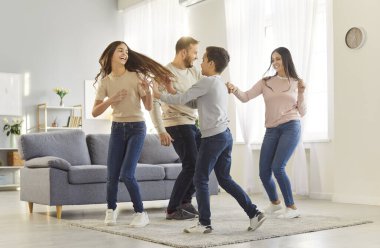 Çocuklarla mutlu bir aile evde eğlenirken neşe ve kahkaha anlarını paylaşıyorlar. Çocuklar ve aileleri enerjik bir şekilde dans ediyorlar, koşuyorlar ve rahat bir oturma odasında halının üzerinde dönüyorlar. Aile kavramı.