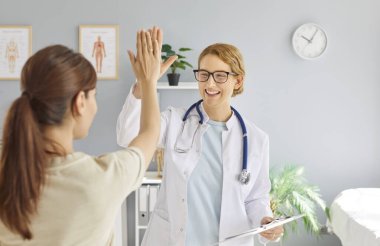 Tedavinin başarısına sevinen mutlu, güler yüzlü kadın doktor, tıbbi muayeneden sonra klinikte ayakta duran hastaya beşlik çakıyor. Sağlık ve Tıp Konsepti.