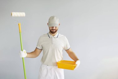 Gülümseyen erkek ressam, inşaat işçisi, hazırlık için üniforma giyen profesyonel tamirci, oda tamiri işlerini bitiren, yenilendikten sonra dairedeki renkli duvar.