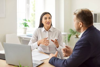 Ofisteki çeşitli çalışanlar takım toplantısında bilgisayar başında beyin fırtınası yaparken konuşuyor, iş adamları iş fikrini tartışmak için dizüstü bilgisayarda birlikte çalışıyorlar, kadın eğitmen de yardım ediyor.