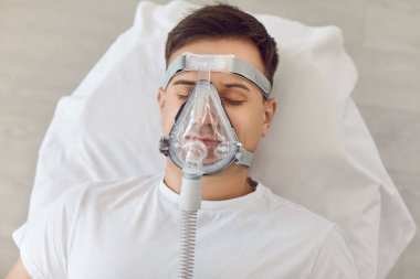 Evde uyuyan, oksijen maskesinden nefes alan bir adam. Astım ya da uyku apnesi için tıbbi tedavi görüyor, evde sağlık ve sağlık hizmetleri sunuyor..