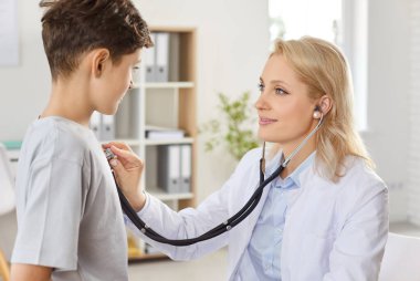 Kadın doktor, erkek ciğerlerini steteskopla dinliyor, yakın plan. Klinikteki çocuk doktoru gençlerin sağlığını kontrol ediyor. Doktor muayenesi, akciğer kontrolü, zatürree, soğuk, öksürük. 