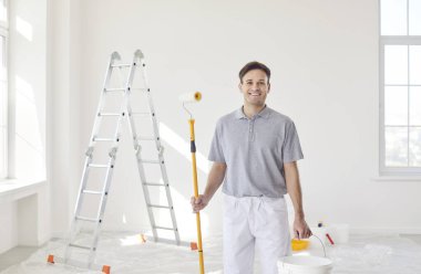 Neşeli ve mutlu bir adamın portresi, profesyonel bir ressam, tadilat sırasında bir evi boyuyor. Yetenekli işçi ev duvarlarına canlı renkler ekleyerek görevine odaklanmış..