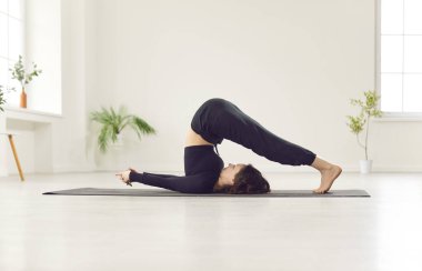 Siyah spor kıyafetleri giyen, yoga yapan, Halasana egzersizi yapan, Plough pozisyonunda duran, ev sporu yapan güzel bir kız ya da sağlıklı bir yaşam tarzı için modern stüdyoda spor yapan bir kadın.