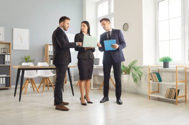 Takım elbiseli üç iş adamı ofis içinde dizüstü bilgisayara bakıyor ve birlikte çalıştıkları web pazarlama projesini tartışıyorlar.