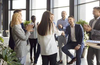 İş adamları, modern ofiste grup toplantısına yeni kadın çalışanları tanıtırlar. İş yerine yeni gelen kişiye hoş geldin derler. Meslektaşları, acemiyi iş tanıtımıyla tebrik ederler.