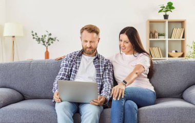 Aile çifti evdeki kanepede rahatlıyor, online eğlence için dizüstü bilgisayar kullanıyorlar. Birlikte zaman geçirmekten, interneti vurgulamaktan, rahatlamaktan ve ev ortamında paylaştıkları anlardan hoşlanırlar..