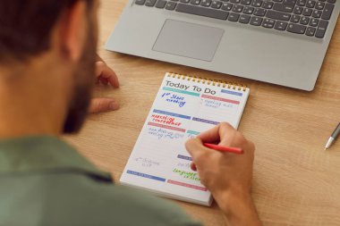 İş adamı planlama görevlerinin en üst görüntüsü ve not defterinde evinde ya da ofisinde dizüstü bilgisayarla oturarak yapılacaklar listesi. Günlük planlarla takvim yapmak isteyen bir adam. İş planlama konsepti.