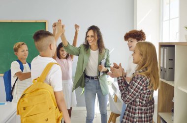 Gülümseyen öğrenciler grubuyla çevrili kendini adamış öğretmen, dersten sonra her öğrenciyle beşlik çakıyor. Sahne, pozitif birlik ve takım çalışmasının özünü yakalıyor..