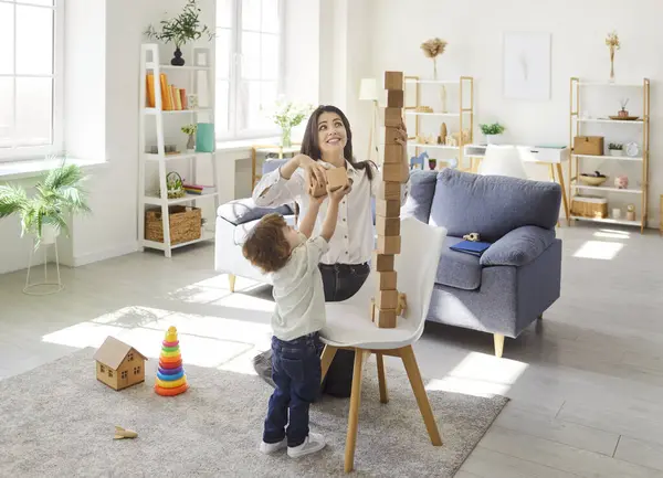Genç, mutlu, gülümseyen bir annenin portresi. Küçük tatlı bir çocukla birlikte evdeki oturma odasında eğitici bir piramit oyunu oynuyor. Aile ve insanlar kavramı.