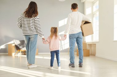 Genç bir aile, heyecan ve beklentiyle yeni satın aldıkları evlerine girer. Ebeveynlerin çocuk ellerini tuttukları ve birlikte oturma odasına yürürken karton kutu taşıdıkları arka manzara..