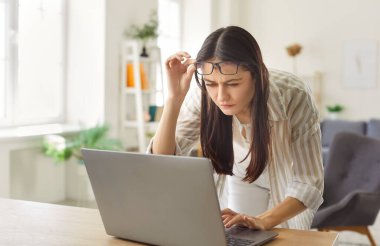 Ofiste dizüstü bilgisayarla çalışan yorgun kadın serbest çalışan, internet görevleri yüzünden görme güçlüğü çeken, yorgunluk ve görsel rahatsızlıkla mücadele eden,.