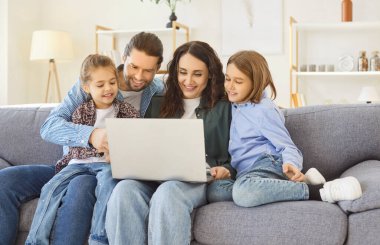 Küçük çocukları olan mutlu ebeveynler yeni dizüstü bilgisayarlarıyla eğleniyorlar, rahat bir oturma odası, çocukları olan sevgi dolu bir çift evde bilgisayar kullanıyor, aile birlikte alışveriş yapıyor, internetten izliyor. 