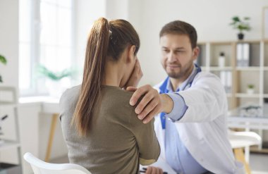Erkek doktor desteği, mutsuz, hasta bir kadın hasta elini omzuna koyuyor. Klinikte oturan hekim muayenede bir kadına danışmanlık yapıyor..