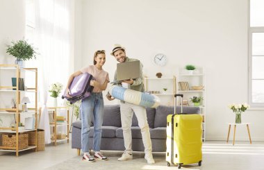 Yaz tatili için sıcak satış arayan genç bir aile, uçuş için online bilet rezervasyonu, dizüstü bilgisayara odaklanma, oturma odasında tam uzunlukta durmak, tatil hazırlıkları.