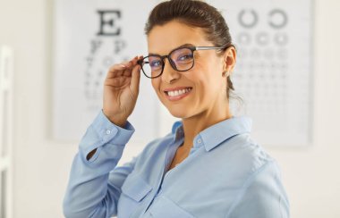 Görüş düzeltmesi için gözlük takmayı öneren mutlu kadın göz doktoru, görme testi kuruluna karşı poz veren klinik hastalarına göz sağlığı teşhisi koyuyor. Optalmoloji kavramı