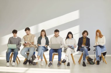 Sınıfta sıra sıra oturan, kitap okuyan ve dizüstü bilgisayarlar üzerinde çalışan odaklanmış genç öğrenciler. İş görüşmesini bekleyen bir grup erkek ve kadın iş arayanlar. İnsan kaynakları, istihdam, eğitim.