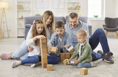 Genç mutlu ebeveynler, anne ve baba çocuklarla birlikte yerde oturuyor ve evdeki oturma odasında eğitici ahşap piramit oyunu oynuyorlar. Aile eğlencesi ve insan konsepti.