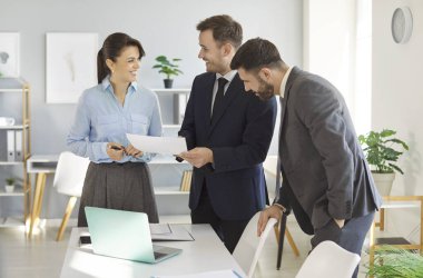 Modern ofiste, üç meslektaş belgeleri incelerken dostane bir tartışmaya giriştiler. Kadın ve iki erkek neşeyle konuşuyor, düşüncelerini paylaşıyor, bir işbirliği ortamı sergiliyorlar..