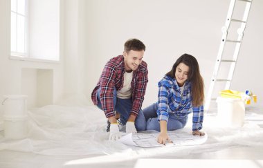 Evde tadilat yapmayı planlayan pozitif bir çift, bir planı inceliyor ve proje stratejisi ve takım çalışmasını tartışıyor. Yeniden yapılanmaya hazırlanıyorlar, birlikte detaylı planlamaya odaklanıyorlar..